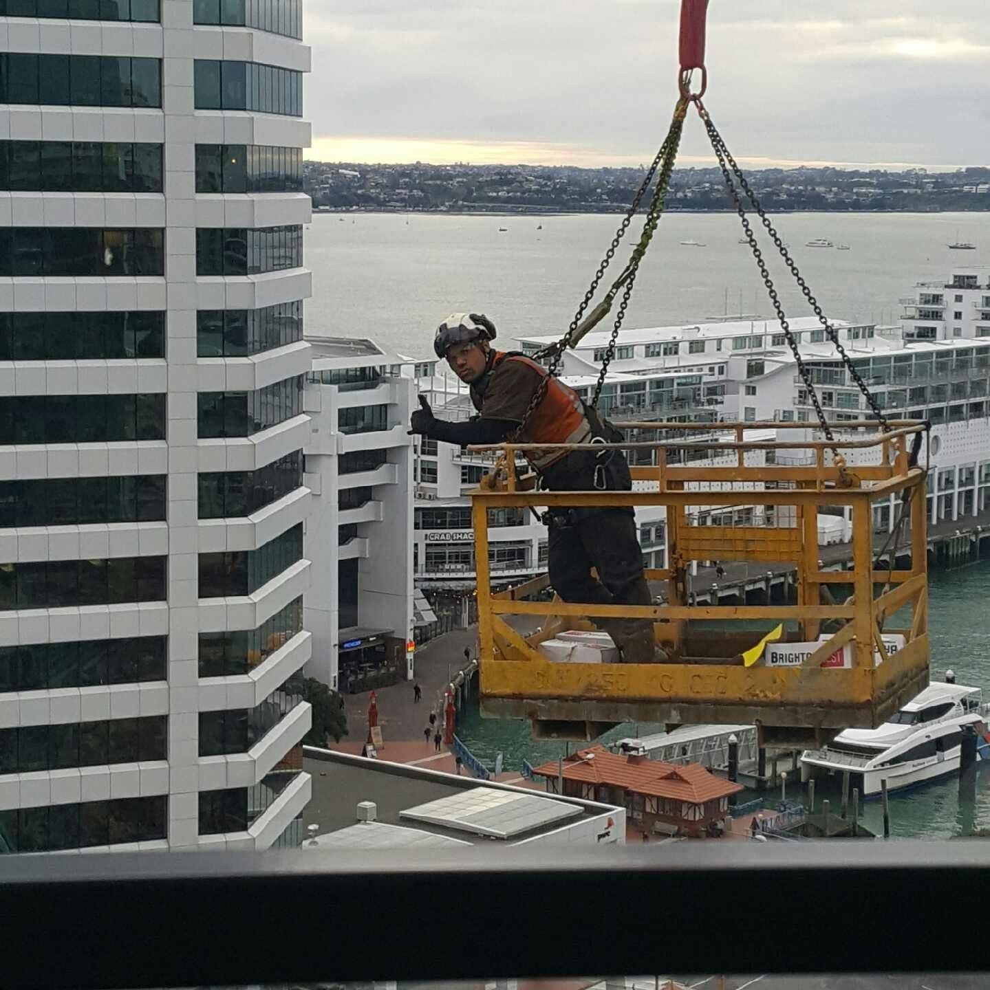 Sonny van Tol working as a dogman/rigger, suspended in a man cage over Auckland waterfront